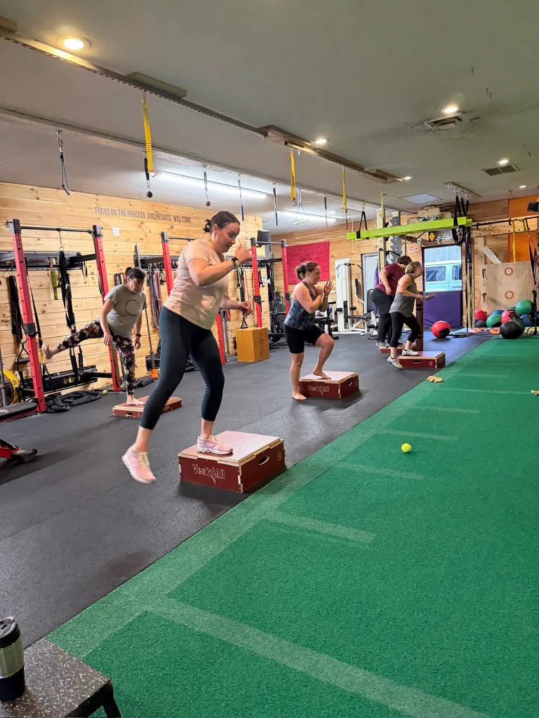 Members stepping up onto plyo boxes on the turf during a coached class